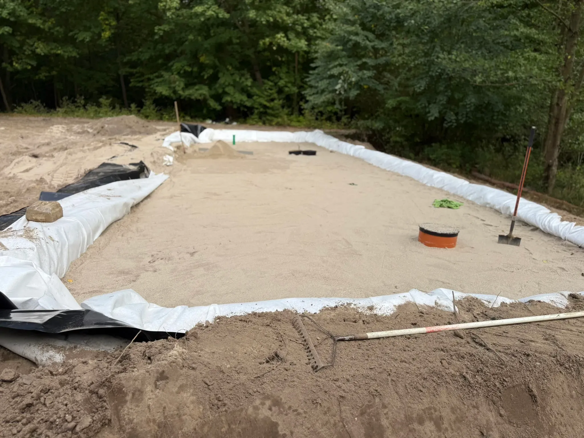 Filterkörper fertig geharkt — die Oberfläche ist eben, im Hintergrund werden die Rohre eingemessen. Als Nächstes folgt die Bepflanzung mit Schilf und Rohrkolben